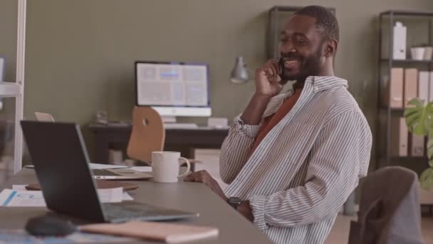 成功したアフリカ系アメリカ人ビジネスマンの中低速ショット現代のオフィスの机に座ってノートパソコンで作業中に電話をかける — ストック動画
