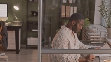 Çizgili gömlekli Afro-Amerikan iş adamının orta yavaş portresi. Geceleri ofiste çalışırken kameraya gülümsüyor.