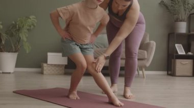 Aktif genç bir kadının, 11 yaşındaki tatlı kızına doğru yoga pozisyonunda durması için yardım ederken, tecrit süresince evde birlikte pratik yaparken yavaş çekimleri.