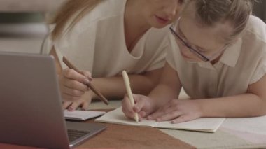 Sevgi dolu bir annenin, 11 yaşındaki kızına okul ödevlerinde yardım ederken, sıcak oturma odasında yerde yan yana yatarken.