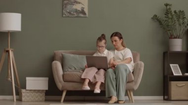 Sevgi dolu bir anne ve 11 yaşındaki kızının kanepede oturup dizüstü bilgisayarda film izlemesi ve kucaklaşması.