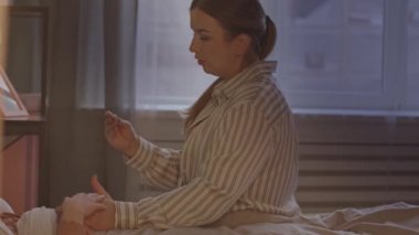 Bakıcı annenin, 11 yaşında hasta bir kızın yatakta yatma sıcaklığını ölçerken ki yavaş çekimi.