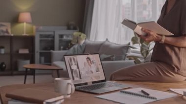 Kitap okurken ve laptopla tıpla ilgili video dersi izlerken, evde ders çalışırken tanınmayan olgun bir kadının yavaş çekimleri.