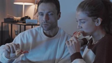 Gecenin geç saatlerinde TV 'de film izlerken pizza yiyen romantik çiftin yavaş çekimi.