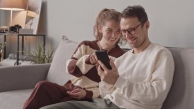 Kafkasyalı genç çiftin evlerindeki kanepede otururken akıllı telefon kullanırken orta yavaş çekimleri.