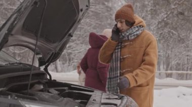 Karlı bir günde arkadaşları yakınlarda beklerken, kış ormanlarında kaputu açık duran genç adamın tamirciye seslenişi orta yavaş bir çekim.