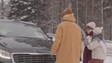 Karlı kış günlerinde dört neşeli çoklu etnik arkadaşın arabaya binip yolculuğa çıkmalarının orta yavaş çekimi.