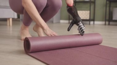 Antrenmandan sonra protez kollu, yoga minderini saran tanınmayan bir kadının yavaş yavaş yakın çekimi.