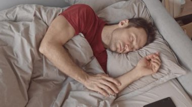 Uykulu, beyaz bir adamın sabah uyandığında ilk önce akıllı telefonunu kontrol edişinin yavaş çekimleri.