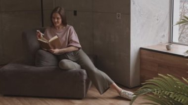 Kafkasyalı, serbest giyinmiş genç bir kadının pencere kenarındaki koltukta oturup ajandasına not aldığı yavaş çekimler.