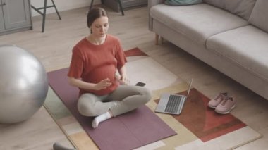 Kafkasyalı hamile kadının evde yoga yaparken dizüstü bilgisayardan video dersleri izlerken çekilmiş yavaş çekimleri.