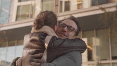 Güneşli bir sonbahar gününde, dışarıda buluşmak için buluşurken kız arkadaşına sarılan yakışıklı beyaz adamın yavaş çekimleri.