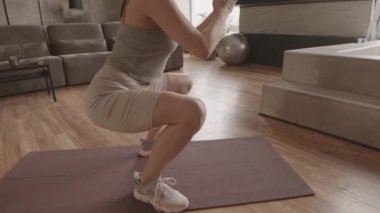 Aktif giyimli, evde eğitim görürken çömelmiş genç bir kadının el kameralı takibi.