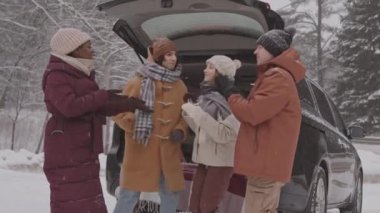 Karlı bir günde, karlı bir günde arabalarının bagajının yanında dans eden dört farklı genç arkadaşın orta yavaş çekimi.