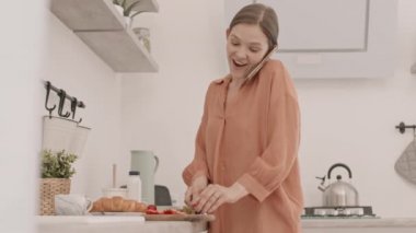 Kafkasyalı genç bir kadının mutfakta kahvaltıda çilek keserken cep telefonuyla sohbet edişinin orta yavaş görüntüsü.