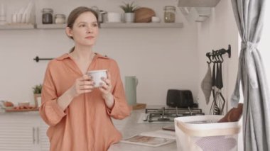 Kafkasyalı genç bir kadının orta yavaş portresi. Elinde bir fincan sıcak kahve ya da kameraya gülümseyen parlak bir mutfak.