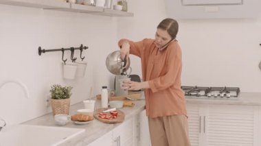 Kahvaltıda cep telefonuyla konuşurken beyaz bir kadının çay yaparken orta yavaş çekimleri.