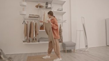 Genç, beyaz bir kadının evde giyecek kıyafet seçerken, aynanın önünde denerken tam boy, yavaş çekim.