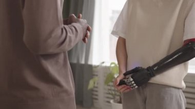 Biyonik kollu beyaz bir kadın ve erkek Afro-Amerikalı arkadaşının kapalı alanda konuşurken çekilmiş yavaş çekimleri.