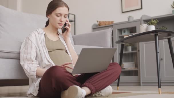 産休中に自宅から仕事をしながら電話をかけ ノートパソコンで入力する若い白人妊婦のスタブショット — ストック動画