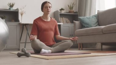 Rahat oturma odasında yoga yaparken yalnız meditasyon yapan, rahat ve genç bir kadının yavaş çekimleri.
