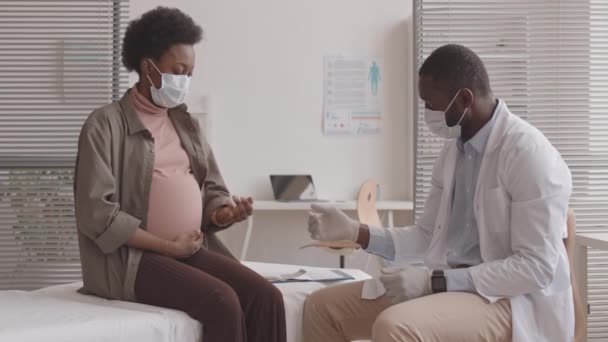 彼の近代的なオフィスで任命中に若いアフリカ系アメリカ人の妊婦のパルスを測定アフリカ系アメリカ人男性医師の中低速ショット — ストック動画