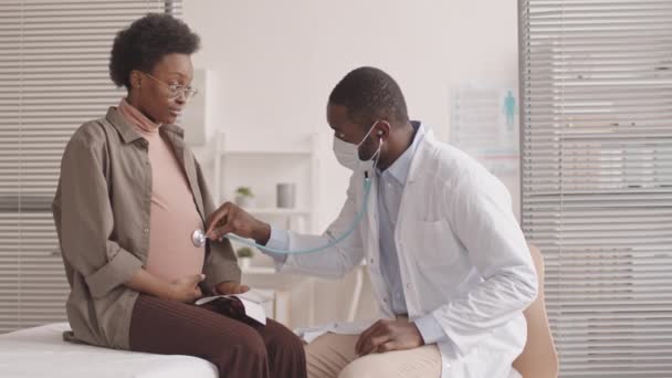 Średnie Powolne Ujęcie Afroamerykańskiego Lekarza Słuchającego Brzucha Młodej Afroamerykanki Ciąży — Wideo stockowe