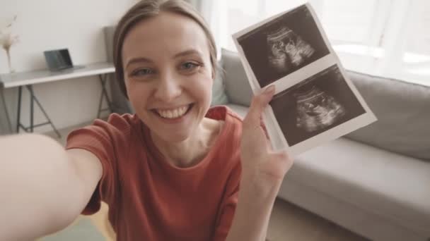 ハンドヘルドハメ撮りスローモショットの幸せな若いです白人妊娠中の女性ショー超音波スキャンの彼女の赤ちゃんにカメラ — ストック動画
