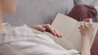 Evdeki kanepede karnını okşarken günlüğe yazan hamile kadının yavaş çekimleri.