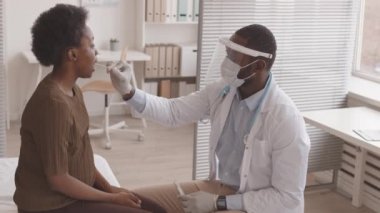 Koruyucu yüz kalkanı ve maskeli bir erkek doktorun hamile bir kadından PCR testi alırken orta yavaş çekimi.