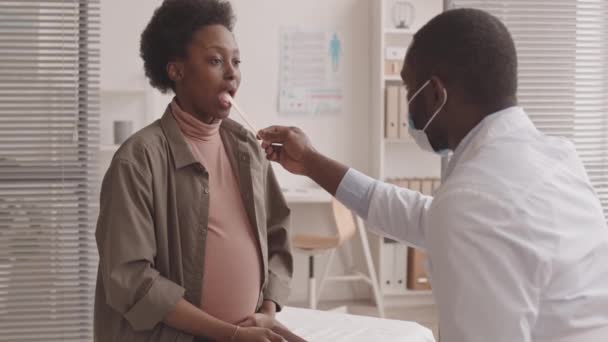 Średnie Powolne Ujęcie Afroamerykańskiego Lekarza Badającego Gardło Młodej Afroamerykanki Ciąży — Wideo stockowe