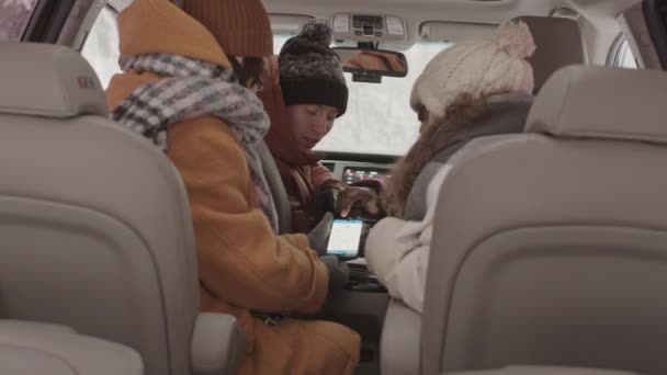 四个年轻的多族裔朋友坐在车里 在智能手机上使用导航应用程序地图 讨论冬季路上要去哪里 拍摄的慢镜头 — 图库视频影像