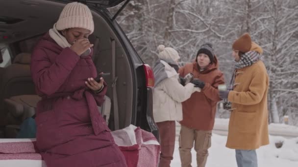 年轻的非洲裔美国女人和她的白人朋友们在冬天的路上一起消磨时光 聊着天 在他们的车旁喝着热茶 慢镜头拍了下来 — 图库视频影像
