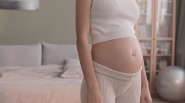 Aktif ve hamile bir annenin evde yoga yaparken karnını okşamasının yavaş çekimleri.