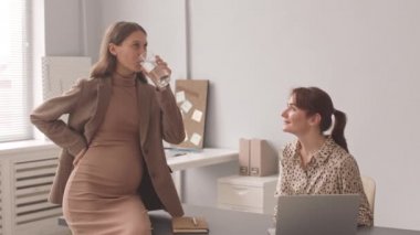 Kafkasyalı hamile bir kadının iş yerindeki kadın meslektaşıyla konuşurken orta yavaş çekimi.