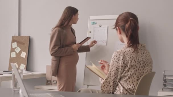 中慢镜头拍摄的年轻白种人怀孕女商人站在白板旁 向计划员的女同事解释工作计划 — 图库视频影像