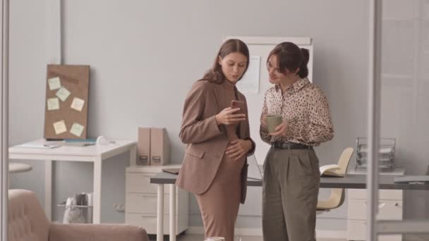中低速ショットの若い白人妊婦ショー赤ちゃん超音波画像上のスマートフォンに彼女の同僚 コーヒーブレイク中に職場に立って — ストック動画