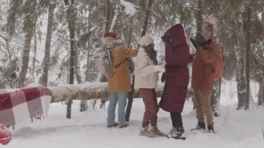 Bir grup arkadaşın kış ormanında birlikte eğlendiği yavaş çekim. Bir adam ağacı sallıyor ve üzerlerine bir sürü kar düşüyor.