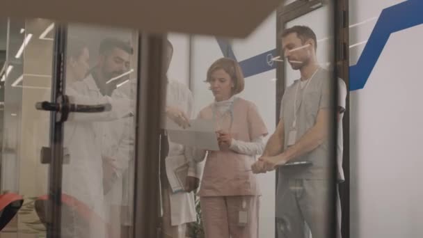 現代病院の廊下に立っている医療文書について議論している5人の多様な男性と女性の医師の中のショット — ストック動画