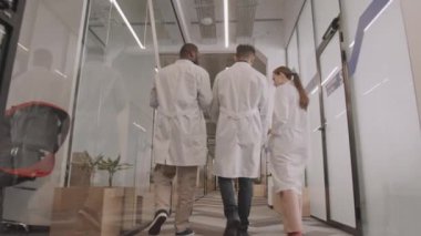Hastane koridorunda yürüyen laboratuvar önlüklü genç doktorların dikiz görüntüsü.