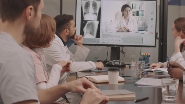 一组年轻的多民族医生通过在线视频会议与女同事讨论病人胸部X光的慢镜头 坐在会议室的桌旁 — 图库视频影像