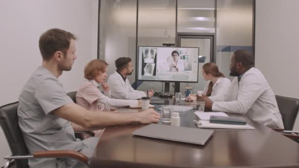 多族裔医疗小组坐在会议室桌旁与女主治医师在线视频会面 讨论病人胸部X光的海豚式摄影 — 图库视频影像