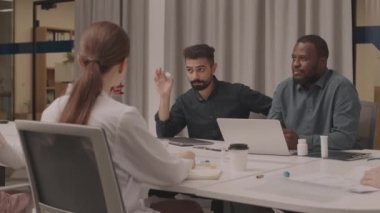 Zekice giyinmiş iki farklı adamın konferans masasındaki toplantılarında bir grup doktora yeni aşıyı sunarken orta boy fotoğrafı.