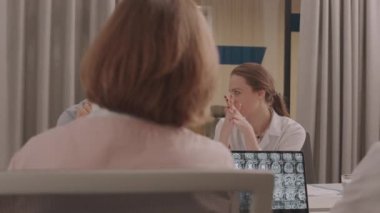 Bir grup erkek ve kadın doktorun toplantı odasında toplanıp dizüstü bilgisayardaki hastanın beyin röntgenini tartışırken orta ölçekli bir görüntüsü.