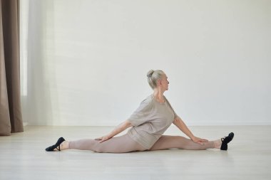 Hanumanasana pozunda oturan aktif yaşlı kadının yan görünüşü