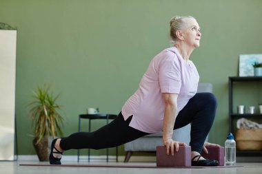 Yoga blokları olan aktif son sınıf öğrencisi bir kadın yerde egzersiz yapıyor.