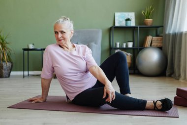 Happy active senior female looking at camera while sitting on mat clipart