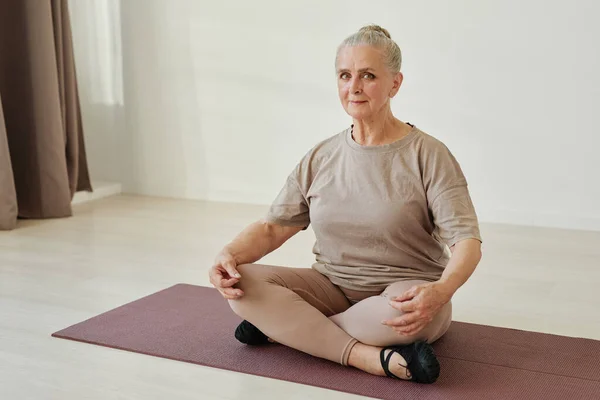 Donna anziana contemporanea in activewear seduta in posizione loto su tappetino — Foto Stock