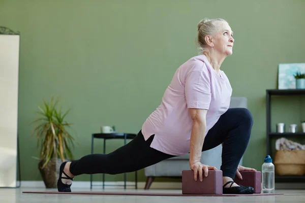 Donna anziana attiva con blocchi di yoga che si esercitano sul pavimento — Foto Stock