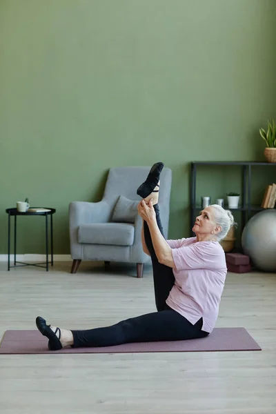 Sportiva senior in t-shirt beige e leggins neri che si esercita sul tappeto — Foto Stock